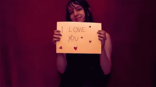 A Woman Is Holding A Piece Of Paper That Says I Love You GIF