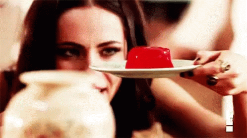 A Woman Is Holding A Plate Of Red Jelly And Looking At It . GIF