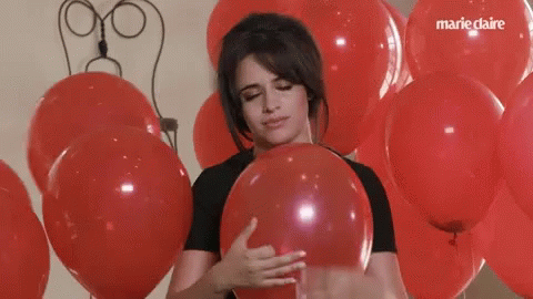 A Woman Is Holding A Red Balloon In Front Of A Bunch Of Red Balloons With Marie Claire Written On The Bottom GIF