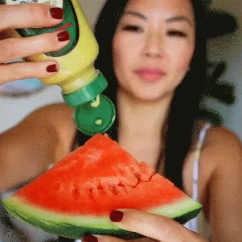 A Woman Is Holding A Slice Of Watermelon With A Bottle Of Mustard On It GIF