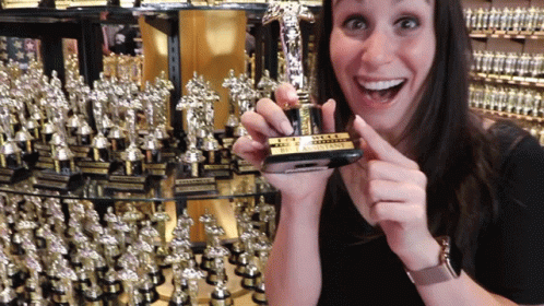 A Woman Is Holding A Small Trophy That Says " The Assistant " GIF