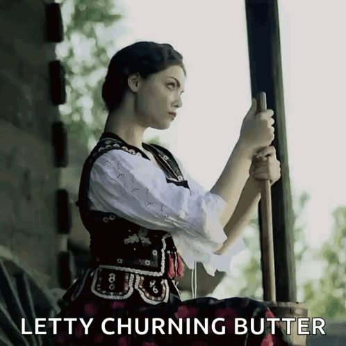 A Woman Is Holding A Stick With The Words Letty Churning Butter Behind Her GIF