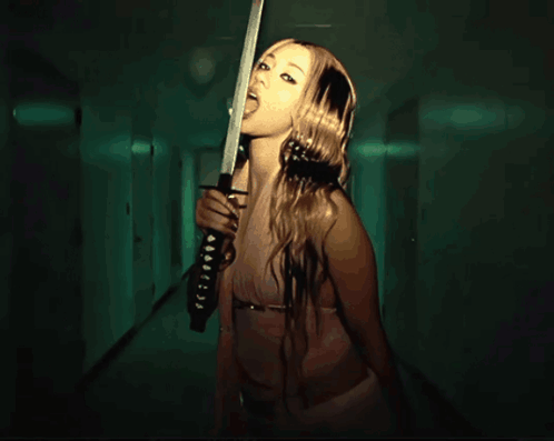 A Woman Is Holding A Sword In A Hallway With A Green Light Behind Her GIF