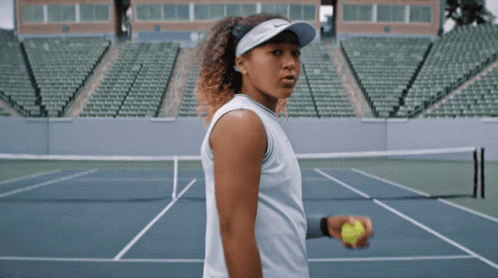 A Woman Is Holding A Tennis Ball On A Court GIF