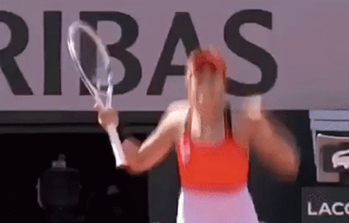 A Woman Is Holding A Tennis Racket In Front Of A Large Sign That Says Ribas . GIF