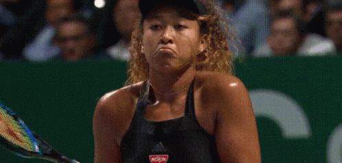 A Woman Is Holding A Tennis Racquet And Making A Funny Face While Playing Tennis . GIF