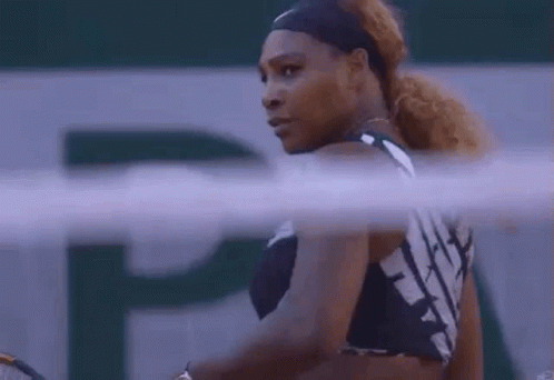 A Woman Is Holding A Tennis Racquet On A Tennis Court And Looking At The Camera . GIF