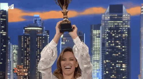 A Woman Is Holding A Trophy In Front Of A City Skyline And The Words The Night Show Are On The Bottom GIF