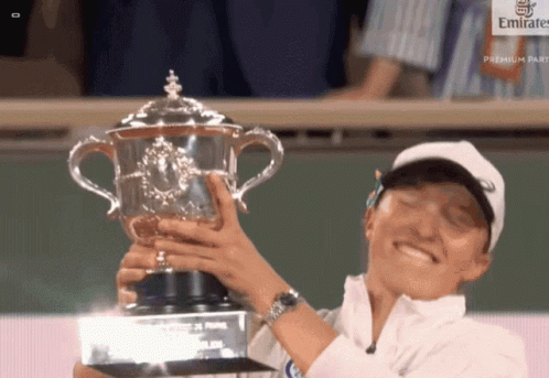 A Woman Is Holding A Trophy In Front Of A Emirates Sign GIF