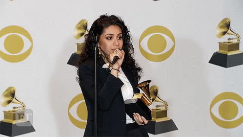 A Woman Is Holding A Trophy In Front Of A Wall With Cbs Logos GIF