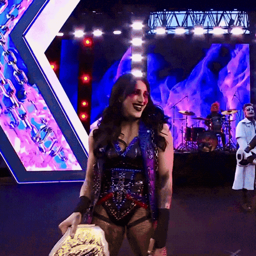 A Woman Is Holding A Trophy On A Stage With A Band Behind Her GIF