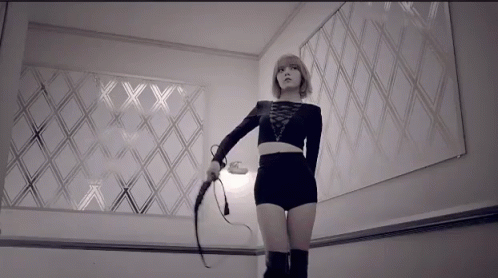 A Woman Is Holding A Whip In Front Of A Wall With The Letters Xx On It GIF
