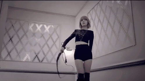 A Woman Is Holding A Whip In Front Of A Wall With The Letters Xx On It GIF
