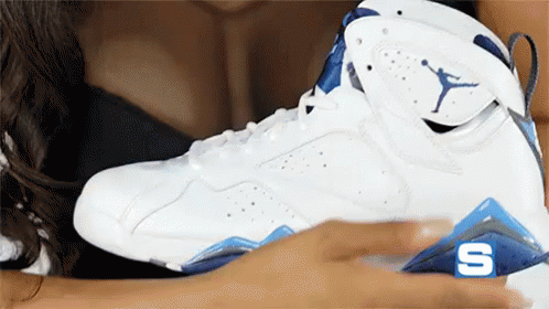 A Woman Is Holding A White And Blue Air Jordan Shoe GIF