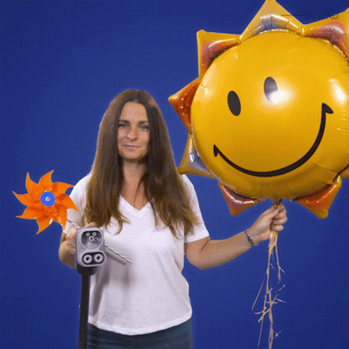 A Woman Is Holding A Windmill And A Balloon With A Smiley Face On It GIF