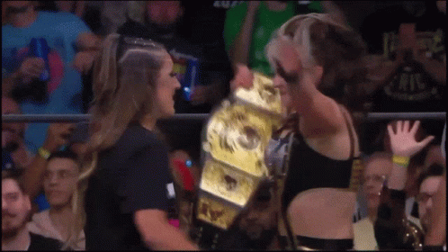 a woman is holding a wrestling championship while another woman watches