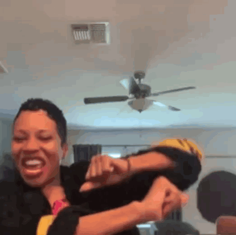A Woman Is Holding Another Woman 'S Arm In A Room With A Ceiling Fan . GIF
