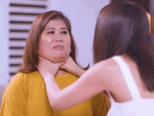 A Woman Is Holding Another Woman 'S Neck In A Room . GIF