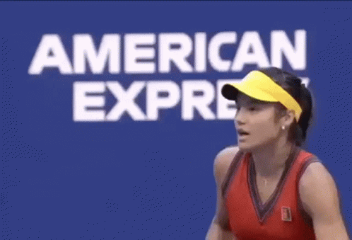 A Woman Is Holding Her Fist Up In The Air In Front Of An American Express Sign . GIF