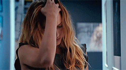 A Woman Is Holding Her Head With Her Hand While Looking At Herself In The Mirror . GIF