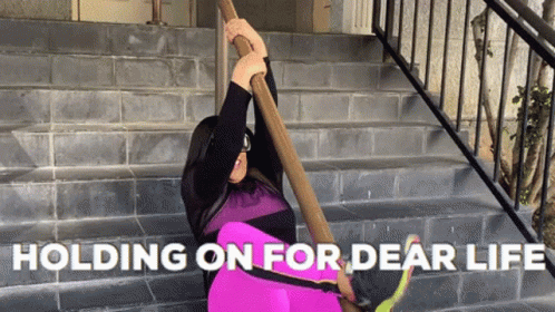 A Woman Is Holding On To A Railing With The Words " Holding On For Dear Life " Above Her GIF