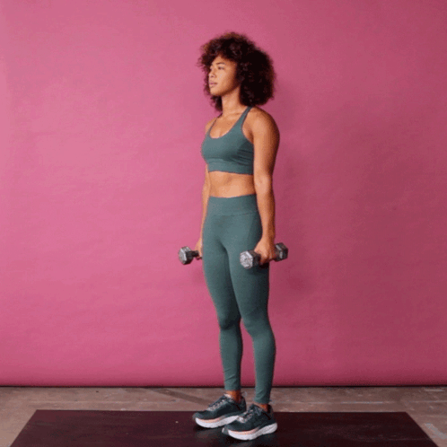A Woman Is Holding Two Dumbbells In Her Hands While Standing On A Mat GIF
