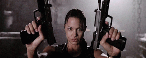 A Woman Is Holding Two Guns In Her Hands In A Dark Room GIF