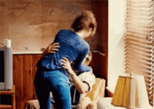 A Woman Is Hugging A Man In A Living Room . GIF