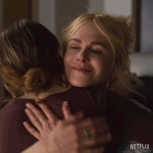 A Woman Is Hugging Another Woman In A Room . GIF