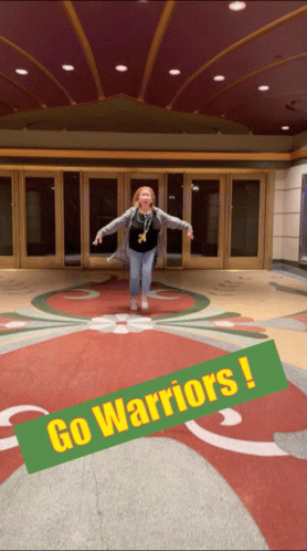 a woman is jumping in front of a building with a sign that says go warriors