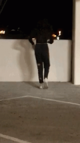 A Woman Is Jumping Over A Wall In A Parking Lot . GIF