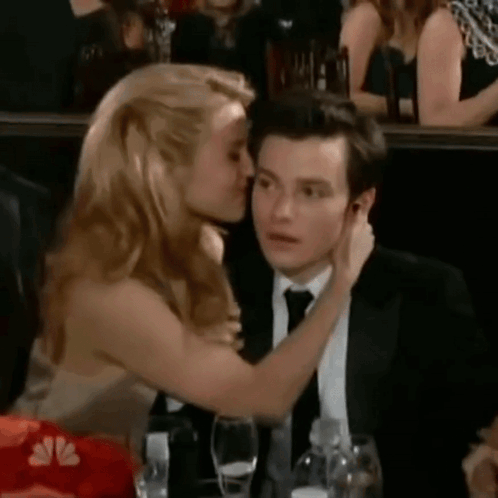 A Woman Is Kissing A Man On The Cheek In A Crowd Of People . GIF