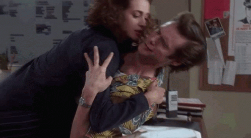 A Woman Is Kissing A Man On The Cheek In A Room . GIF