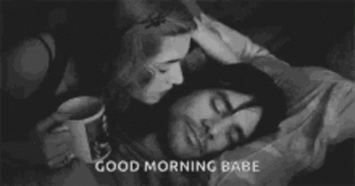 A Woman Is Kissing A Man On The Forehead While He Sleeps In Bed . GIF