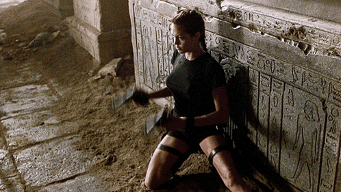 A Woman Is Kneeling Down In Front Of A Wall That Says Egyptian Hieroglyphics GIF