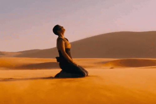 A Woman Is Kneeling Down In The Desert Looking Up GIF