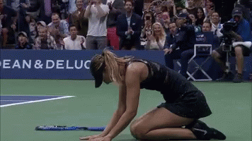 A Woman Is Kneeling Down On A Tennis Court In Front Of A Banner That Says Bean & Deluca GIF