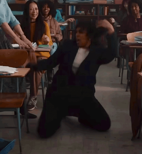 A Woman Is Kneeling On The Floor In A Classroom With Other People GIF