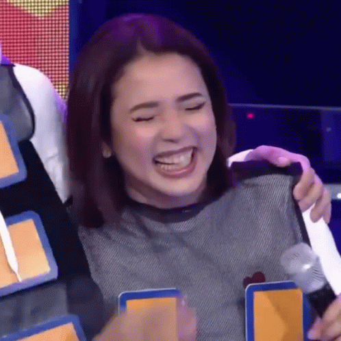 A Woman Is Laughing And Holding A Microphone While Sitting On A Stage . GIF