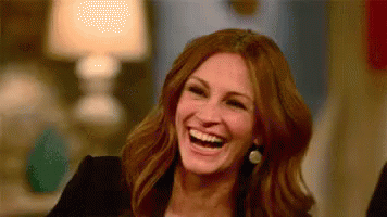 A Woman Is Laughing And Smiling While Sitting At A Table . GIF