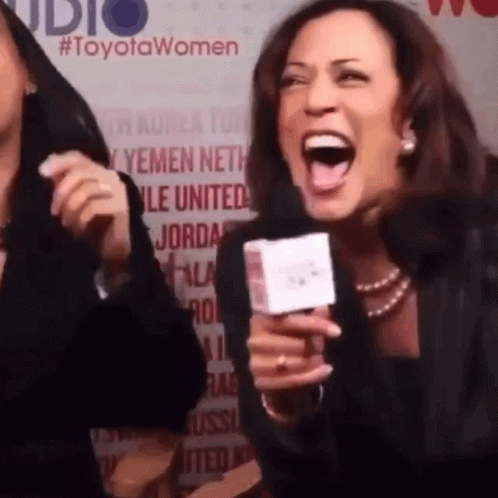 A Woman Is Laughing While Holding A Microphone In Front Of A Toyota Women Sign GIF