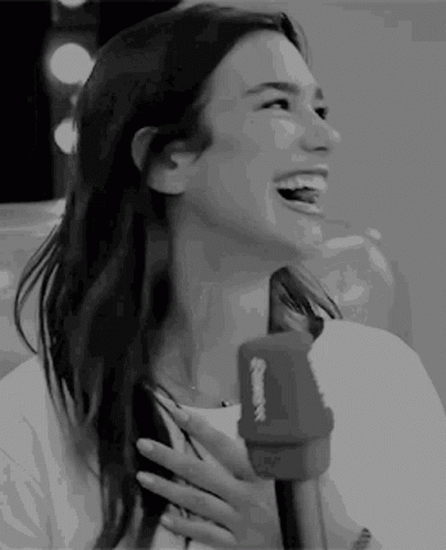 A Woman Is Laughing While Holding A Microphone In Her Hand . GIF