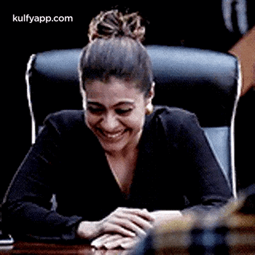 A Woman Is Laughing While Sitting At A Table With Her Hands On Her Lap . GIF