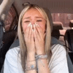 A Woman Is Laughing While Sitting In A Car With Her Hands Over Her Mouth . GIF