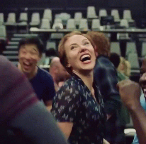A Woman Is Laughing While Sitting In A Crowd Of People . GIF