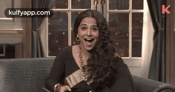 A Woman Is Laughing While Sitting On A Couch . GIF