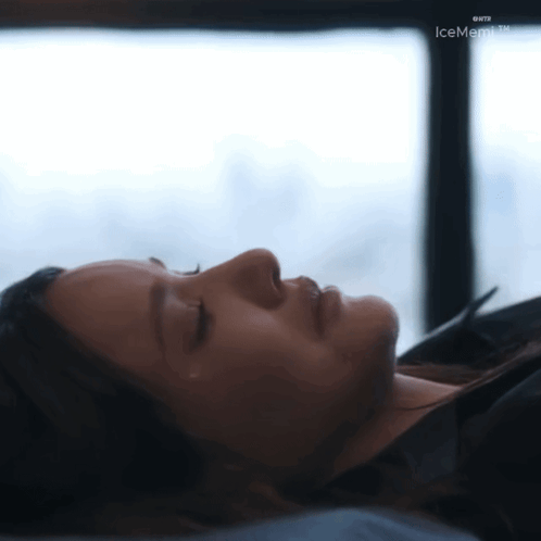 A Woman Is Laying Down With Her Eyes Closed In Front Of A Window With Icememo.tv Written On The Bottom GIF