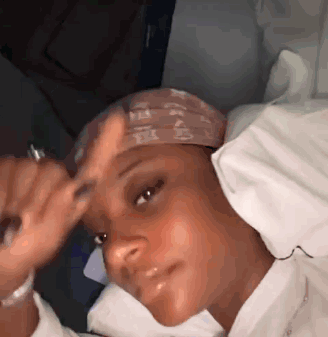 A Woman Is Laying In A Bed With A Bandana On Her Head And Looking At The Camera . GIF