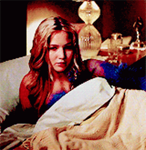 A Woman Is Laying In A Bed With A Lamp In The Background GIF