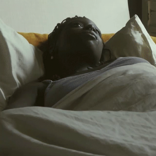 A Woman Is Laying In A Bed With A White Blanket GIF